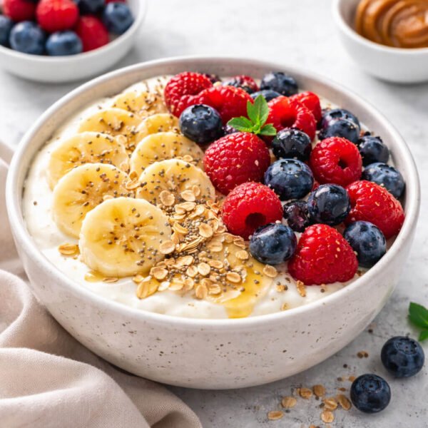 Yogurt berry bowl with banana slices, fresh berries, oats, chia seeds and honey in a ceramic bowl, natural daylight, no-cook breakfast.
